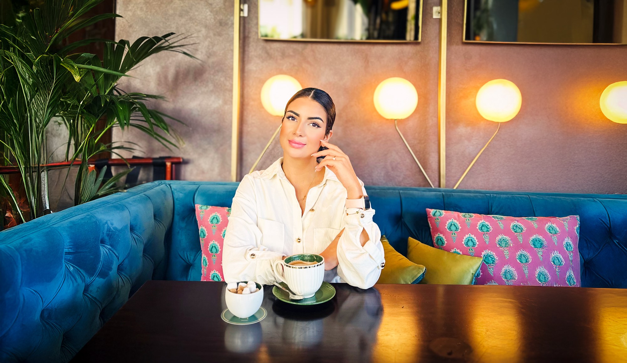 Sobia Mohammed sitzt mit einer Tasse an einem Tisch auf einem blauen Sofa in einem Café